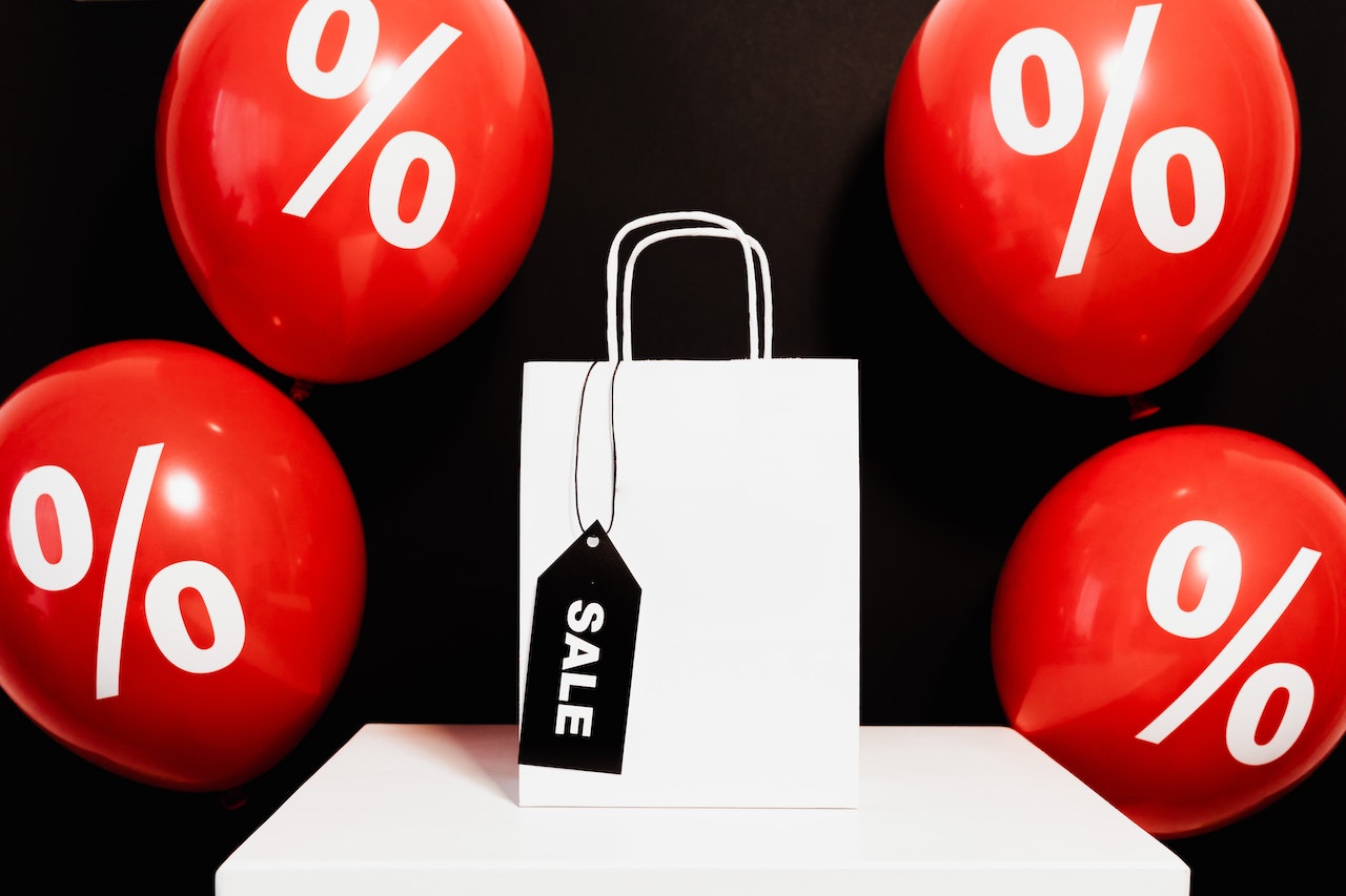 Shopper - Uma bolsa branca em um fundo preto com balões vermelhos com o símbolo de porcentagem