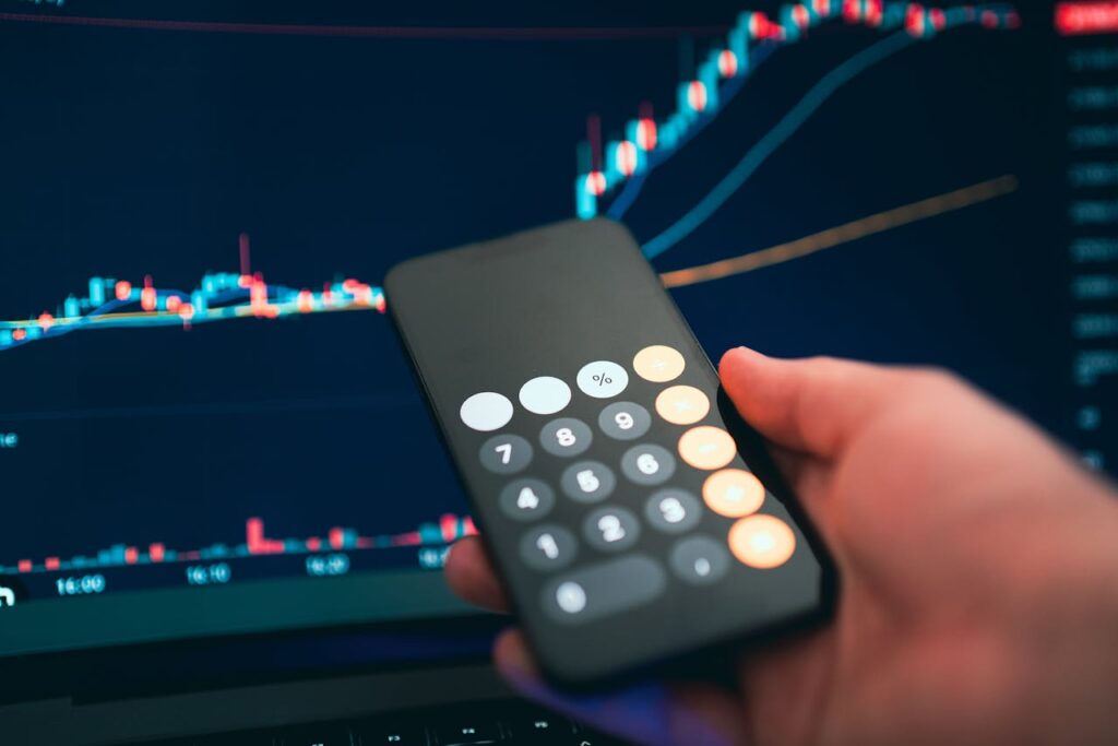 Gestão de receitas - Pessoa segurando o celular com a calculadora aberta e gráficos ao fundo